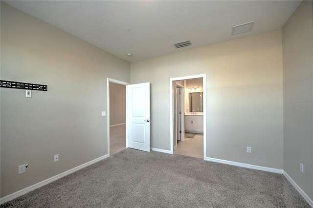 unfurnished bedroom with ensuite bath and light colored carpet