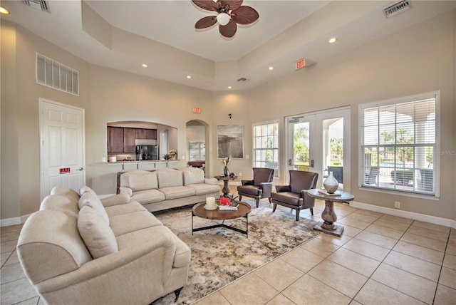 living room featuring ceiling fan, a towering ceiling, light tile patterned floors, and a healthy amount of sunlight