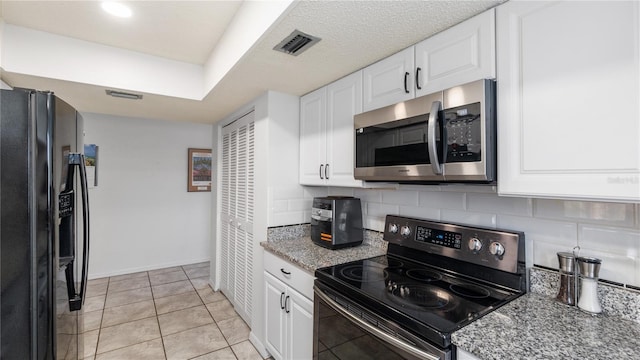 kitchen with black appliances, white cabinets, light stone countertops, light tile patterned floors, and tasteful backsplash