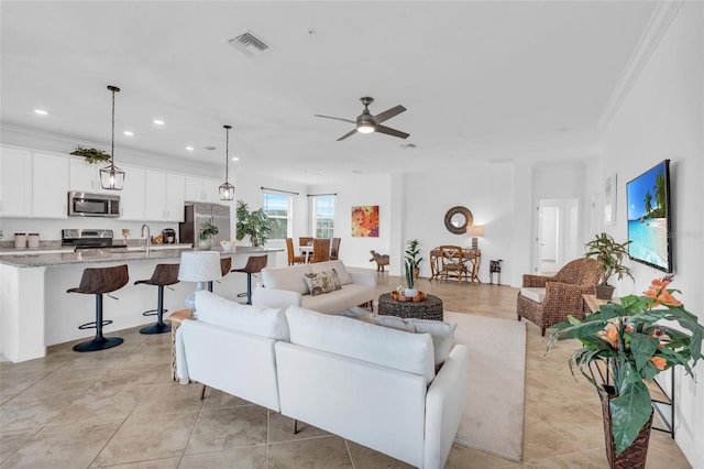 living room featuring light tile patterned floors, ceiling fan, ornamental molding, and sink