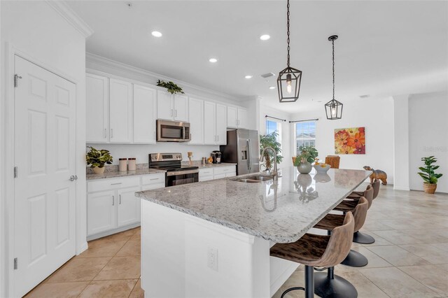 kitchen with stainless steel appliances, a center island with sink, light stone counters, and decorative light fixtures