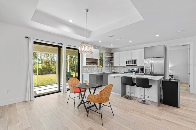 kitchen with appliances with stainless steel finishes, a tray ceiling, pendant lighting, gray cabinets, and a kitchen island