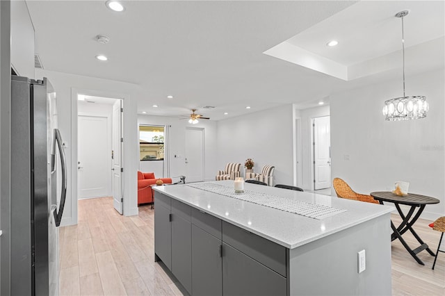 kitchen with light wood-type flooring, ceiling fan, stainless steel fridge with ice dispenser, a kitchen island, and hanging light fixtures