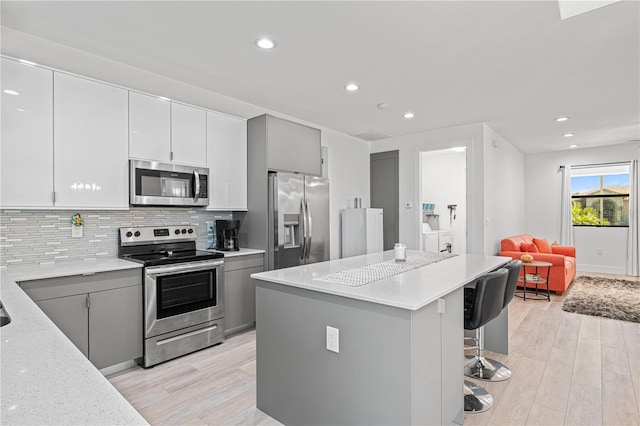 kitchen with gray cabinets, light stone counters, stainless steel appliances, and a breakfast bar area