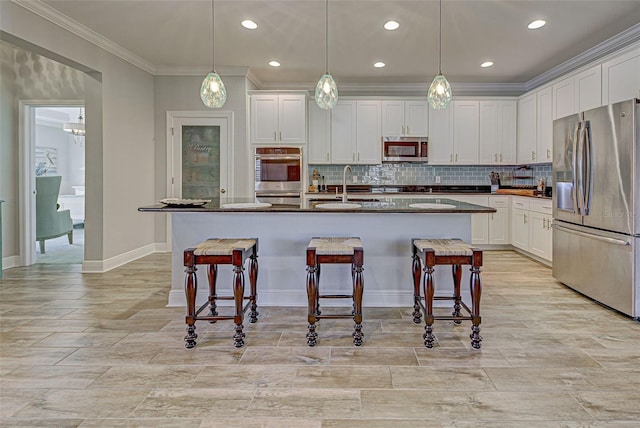 kitchen featuring a center island with sink, decorative light fixtures, a kitchen bar, white cabinetry, and stainless steel appliances