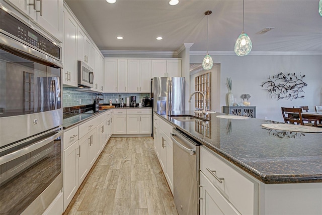 kitchen featuring appliances with stainless steel finishes, a kitchen island with sink, sink, dark stone countertops, and white cabinets