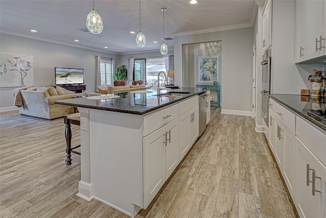 kitchen featuring stainless steel dishwasher, pendant lighting, a center island with sink, white cabinetry, and a breakfast bar area