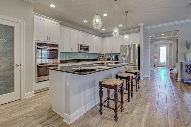 kitchen featuring white cabinetry, stainless steel appliances, tasteful backsplash, an island with sink, and pendant lighting