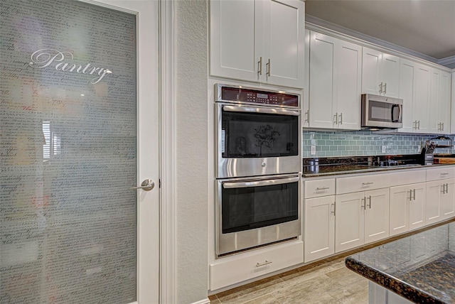 kitchen with dark stone countertops, decorative backsplash, white cabinets, and appliances with stainless steel finishes