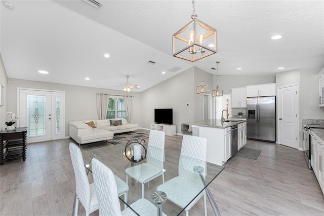 dining area featuring lofted ceiling, ceiling fan with notable chandelier, sink, a textured ceiling, and light hardwood / wood-style floors