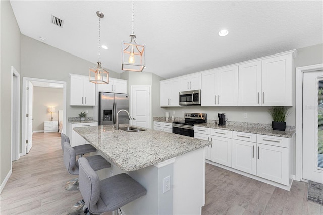 kitchen featuring stainless steel appliances, sink, pendant lighting, white cabinets, and an island with sink