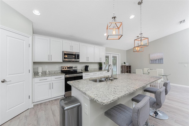 kitchen featuring sink, an island with sink, decorative light fixtures, white cabinets, and appliances with stainless steel finishes