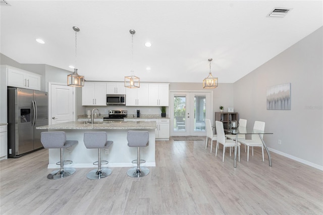 kitchen featuring stainless steel appliances, light stone counters, an island with sink, decorative light fixtures, and white cabinets