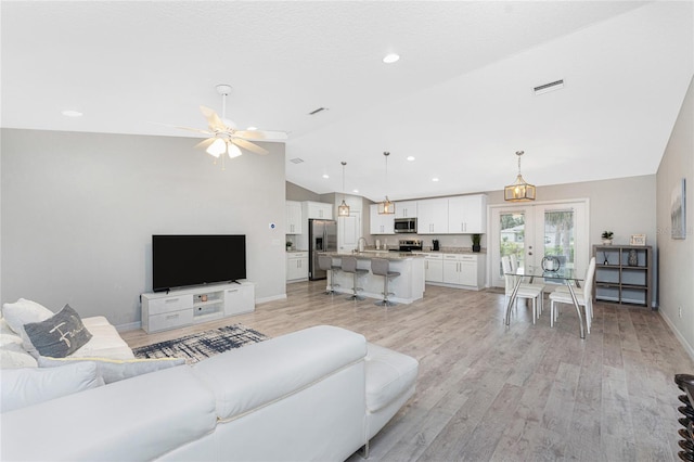 living room featuring french doors, ceiling fan with notable chandelier, light hardwood / wood-style floors, and lofted ceiling