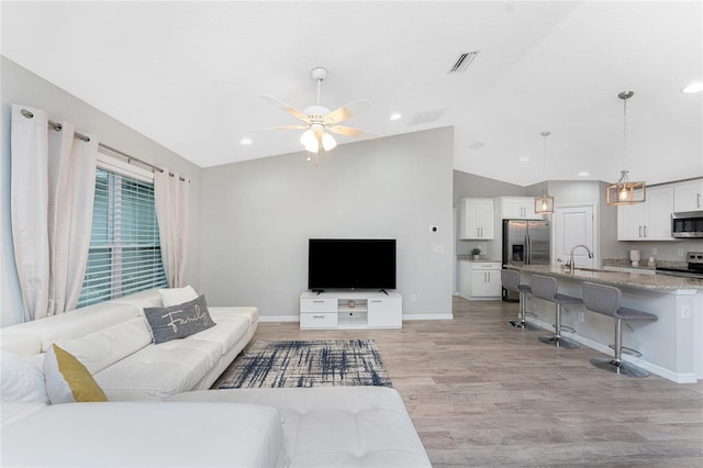 living room featuring ceiling fan, vaulted ceiling, sink, and light hardwood / wood-style flooring