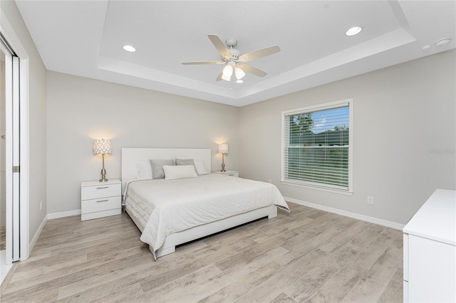 bedroom with a raised ceiling, ceiling fan, and light wood-type flooring