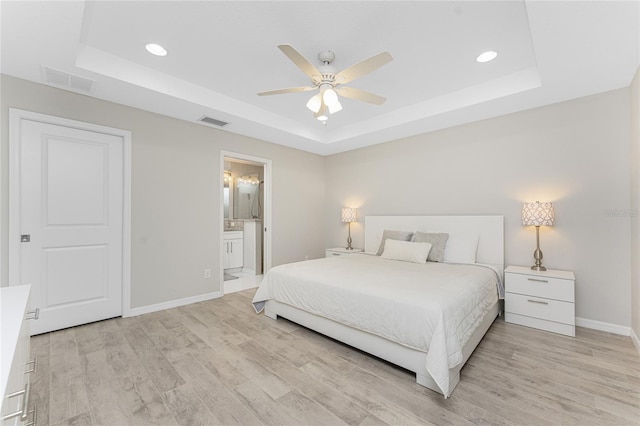 bedroom featuring ceiling fan, light hardwood / wood-style floors, connected bathroom, and a tray ceiling