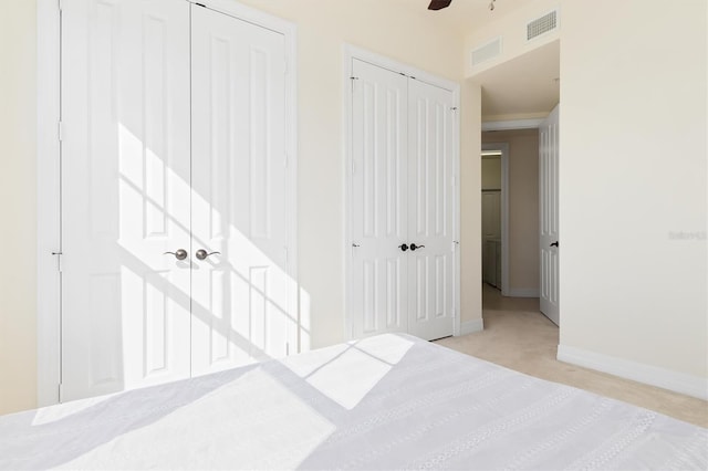 unfurnished bedroom with ceiling fan, light colored carpet, and multiple closets