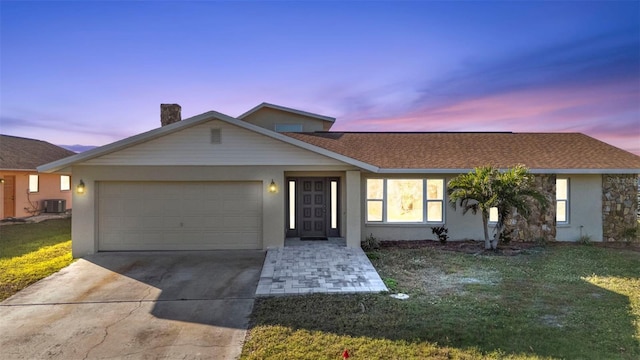 ranch-style home featuring a garage, a yard, and central AC unit