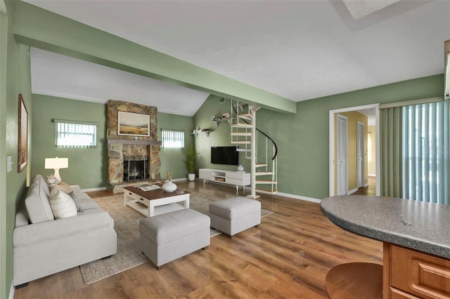 living room with vaulted ceiling with beams, a stone fireplace, and hardwood / wood-style flooring