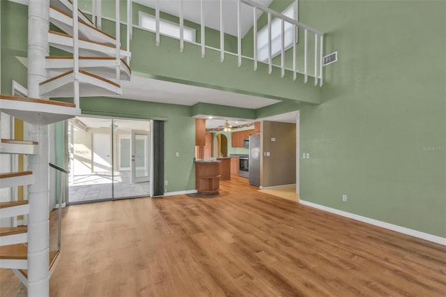 unfurnished living room with a high ceiling, ceiling fan, and light hardwood / wood-style flooring