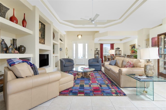 tiled living room featuring a raised ceiling, ceiling fan, built in features, and crown molding