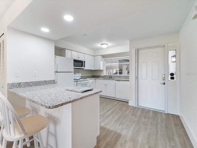 kitchen with white appliances, white cabinetry, light hardwood / wood-style floors, kitchen peninsula, and a breakfast bar area