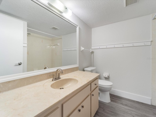 bathroom with vanity, a textured ceiling, a shower, hardwood / wood-style floors, and toilet