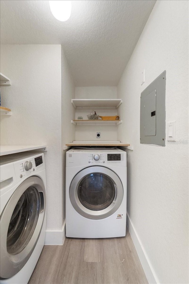 clothes washing area with electric panel, light wood-type flooring, a textured ceiling, and independent washer and dryer