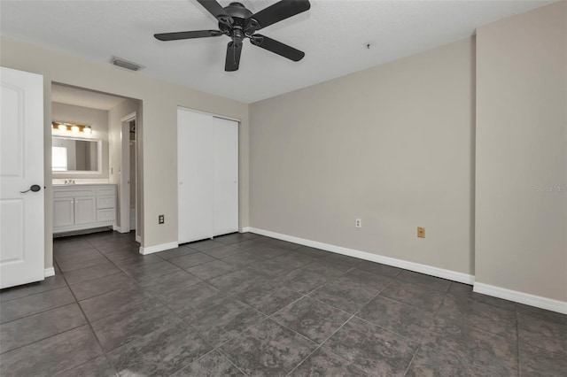 unfurnished bedroom featuring dark tile patterned flooring, a closet, ensuite bath, and ceiling fan