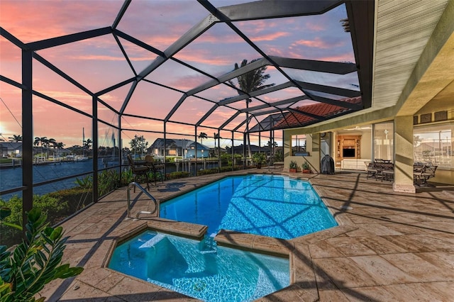 pool at dusk featuring glass enclosure, an in ground hot tub, a water view, and a patio