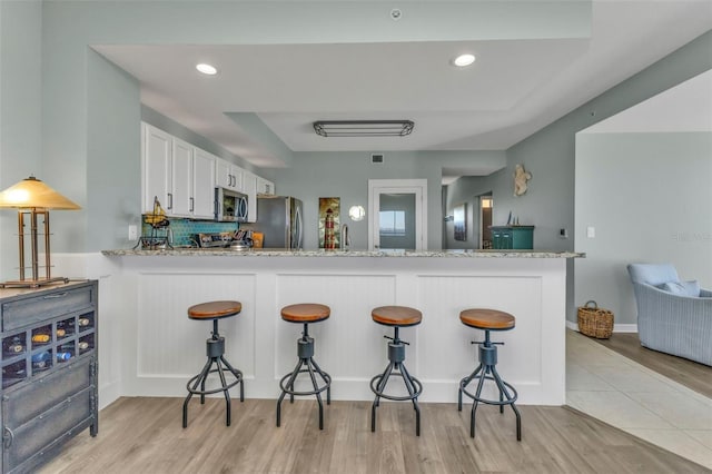 kitchen with stainless steel appliances, white cabinets, light stone counters, and kitchen peninsula