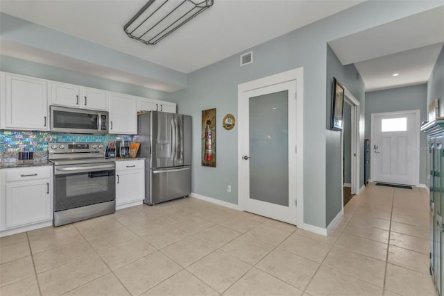 kitchen featuring light tile patterned floors, backsplash, stainless steel appliances, white cabinets, and dark stone counters