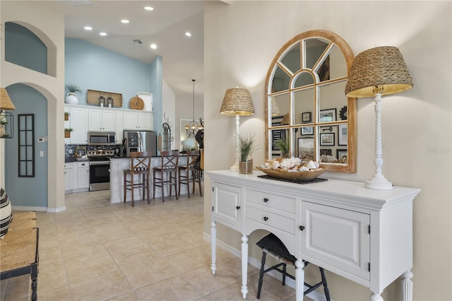 interior space featuring appliances with stainless steel finishes, tasteful backsplash, white cabinets, a high ceiling, and a breakfast bar area