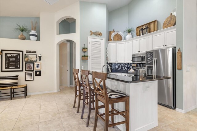 kitchen featuring white cabinetry, a towering ceiling, a kitchen bar, a kitchen island with sink, and appliances with stainless steel finishes