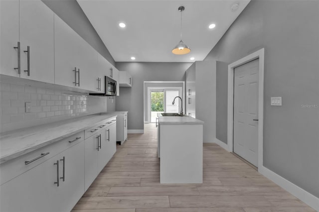 kitchen featuring backsplash, a center island with sink, pendant lighting, sink, and white cabinetry