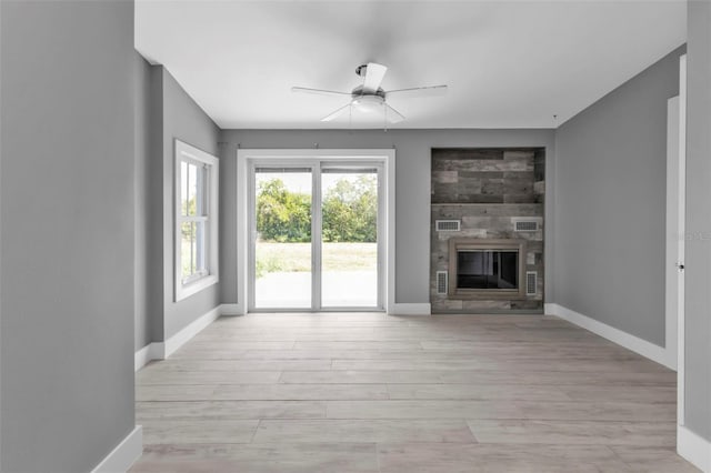 unfurnished living room with ceiling fan, a large fireplace, and light hardwood / wood-style flooring