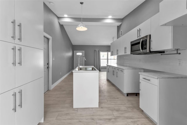 kitchen with white cabinets, tasteful backsplash, sink, hanging light fixtures, and a center island with sink