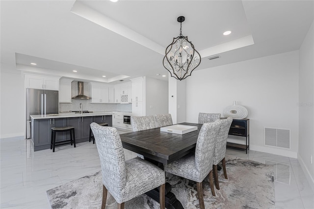 dining area with sink, a raised ceiling, and a chandelier