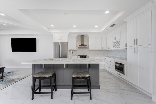 kitchen featuring a raised ceiling, a kitchen breakfast bar, a large island, stainless steel appliances, and wall chimney range hood