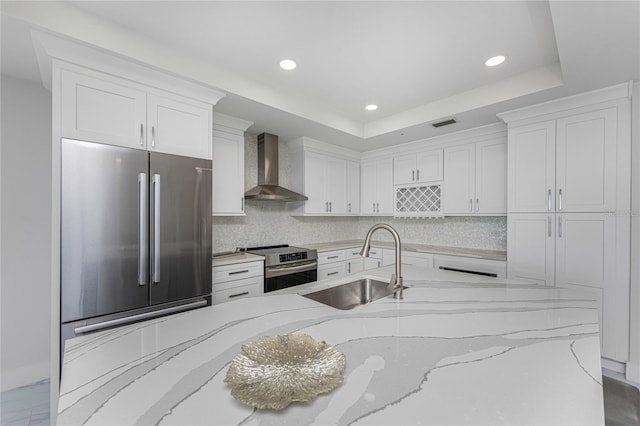 kitchen with sink, wall chimney range hood, stainless steel appliances, light stone countertops, and white cabinets