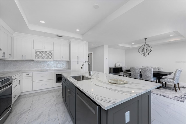 kitchen featuring sink, a tray ceiling, an island with sink, and range