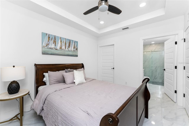 bedroom featuring a tray ceiling, ensuite bath, and ceiling fan