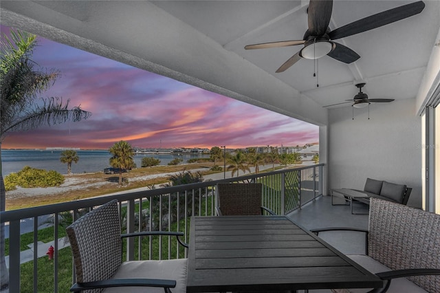 balcony at dusk featuring ceiling fan and a water view