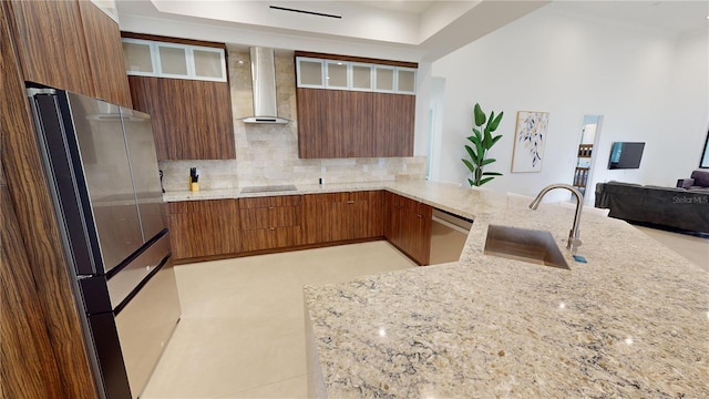 kitchen with light stone countertops, sink, stainless steel appliances, wall chimney range hood, and kitchen peninsula