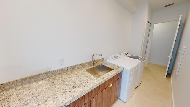 clothes washing area with washer and clothes dryer, cabinets, and sink