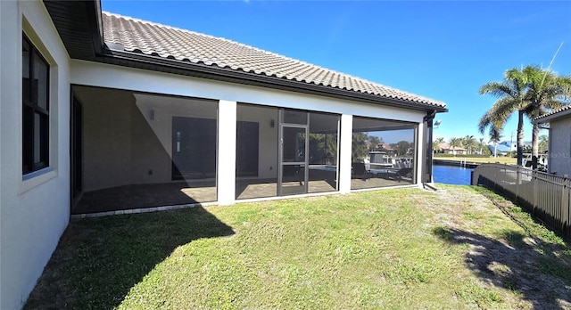 back of property with a sunroom, a water view, and a lawn