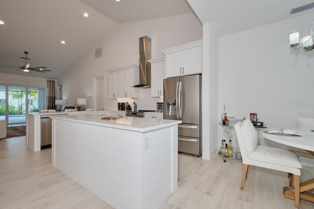 kitchen featuring ceiling fan, stainless steel appliances, wall chimney range hood, vaulted ceiling, and white cabinets