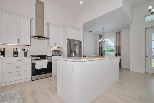 kitchen featuring white cabinetry, wall chimney exhaust hood, decorative light fixtures, a kitchen island, and appliances with stainless steel finishes