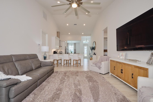 living room with ceiling fan with notable chandelier, light wood-type flooring, and high vaulted ceiling